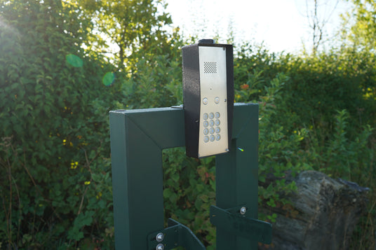 Gate access keypad on a post beside a hedge